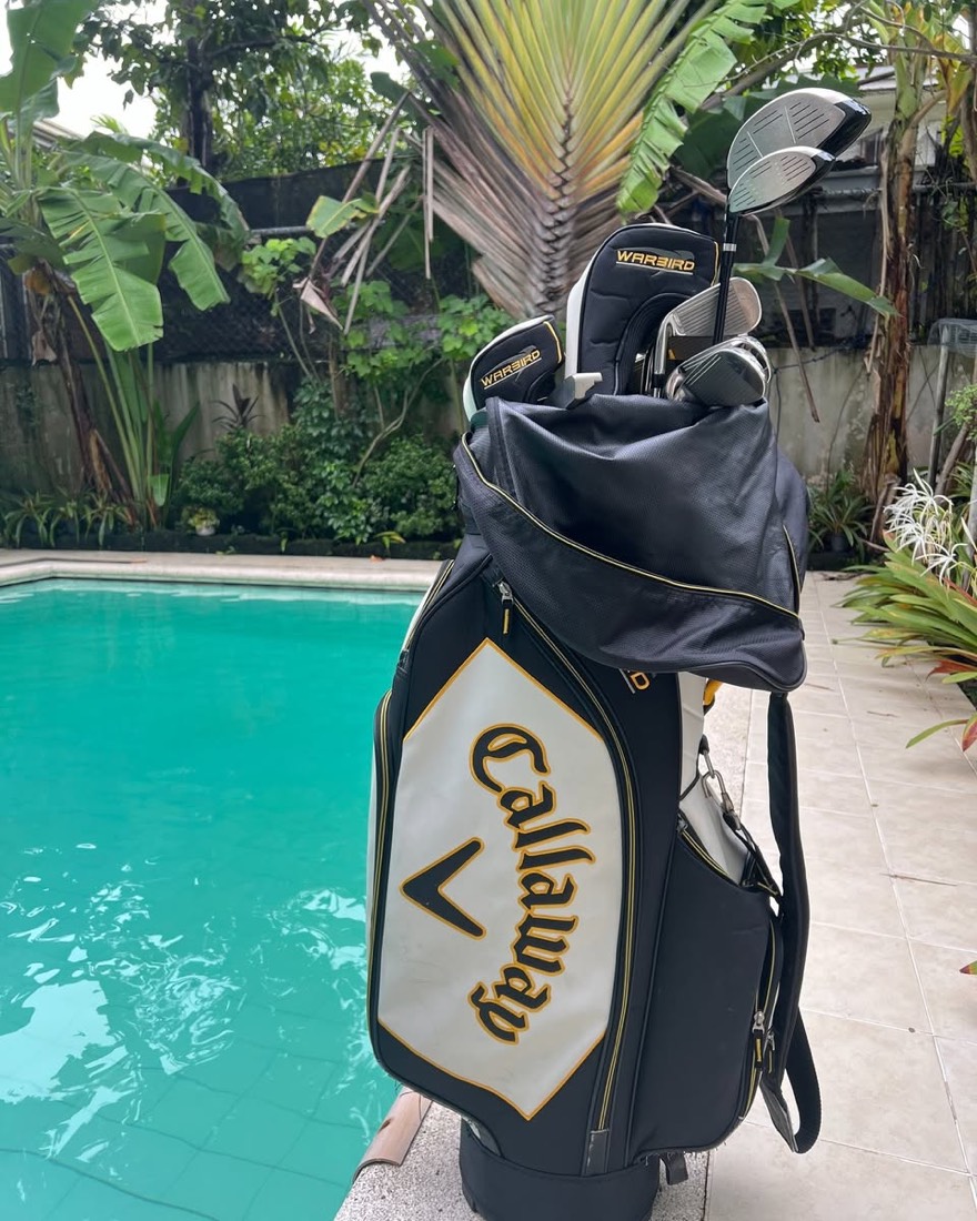 A black, white and gold Callaway cart bag with Warbird headcovers and a driver, photographed poolside.