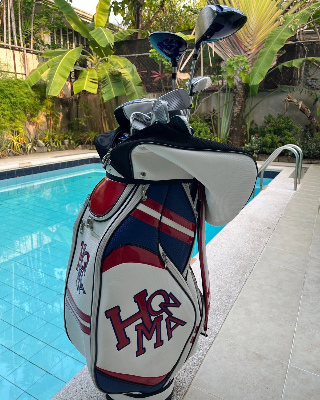 A Honma cart bag filled with a full set of clubs, photographed poolside in daylight.