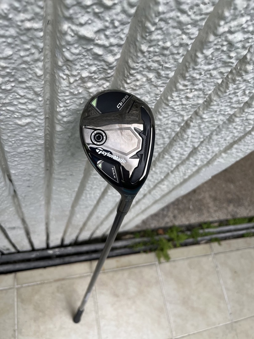 A TaylorMade Qi35 Max rescue club resting against a white gate.