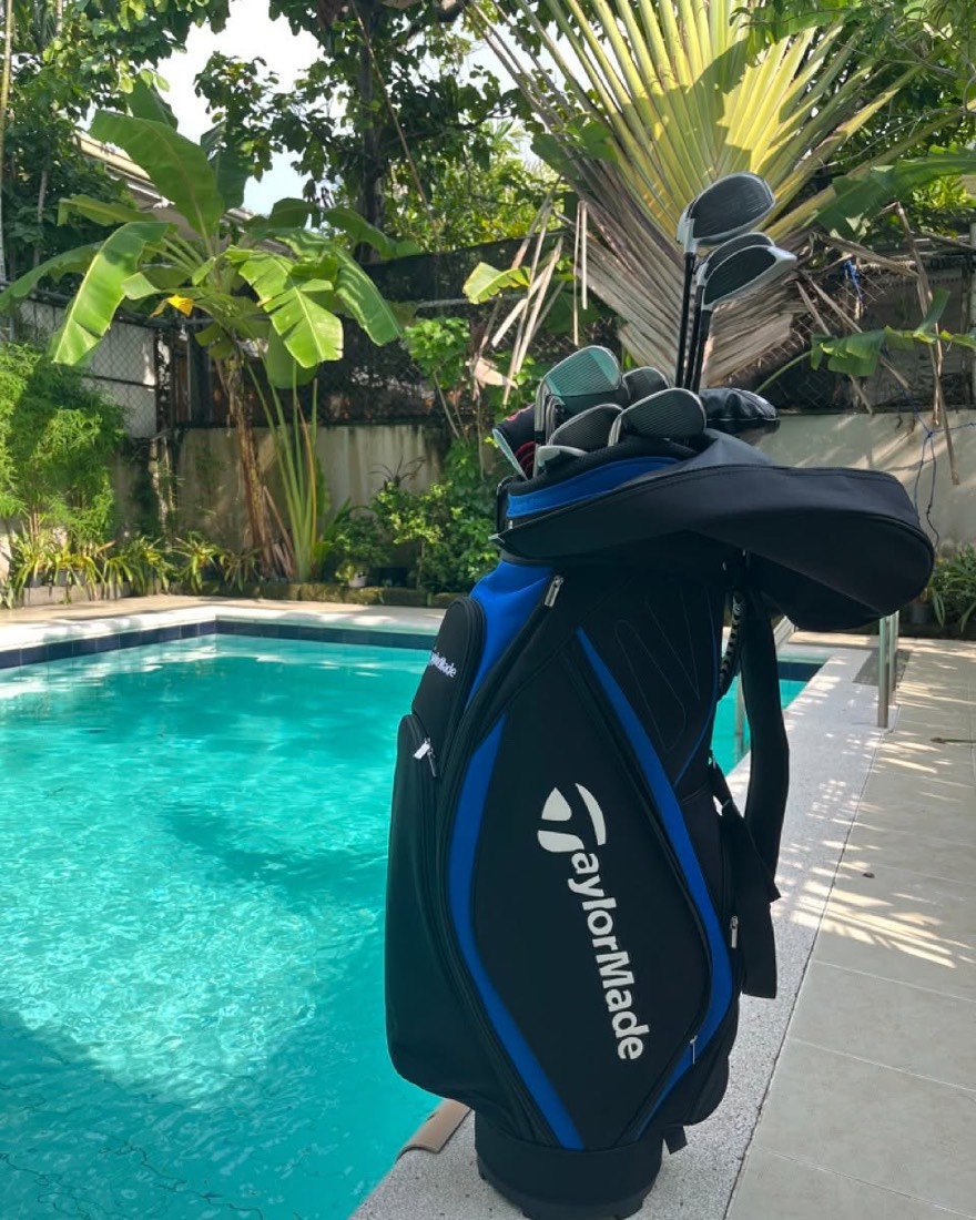 A black and blue TaylorMade cart bag holding a full set of woods and irons, photographed poolside.
